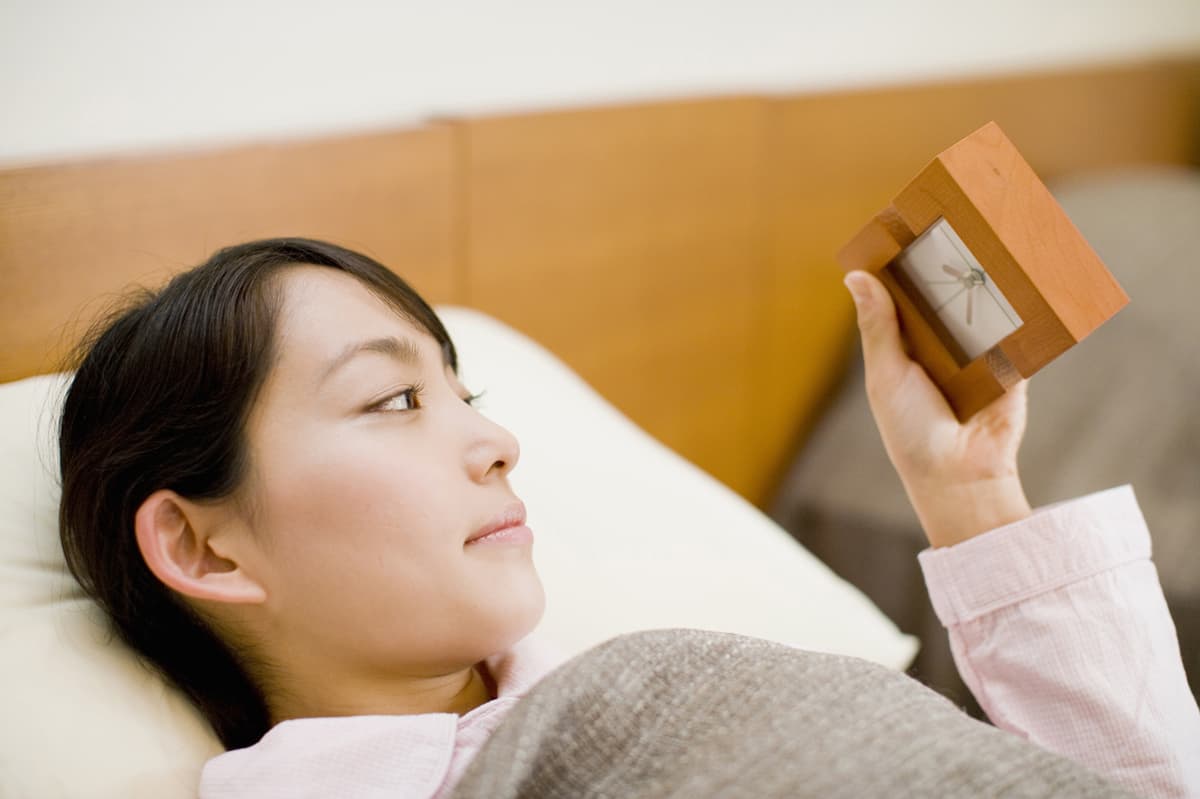 ベッドに寝っ転がり時計を確認する女性